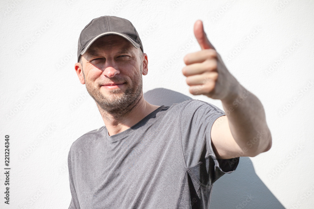 brutal man with a bristle shows an approving gesture against a white wall background