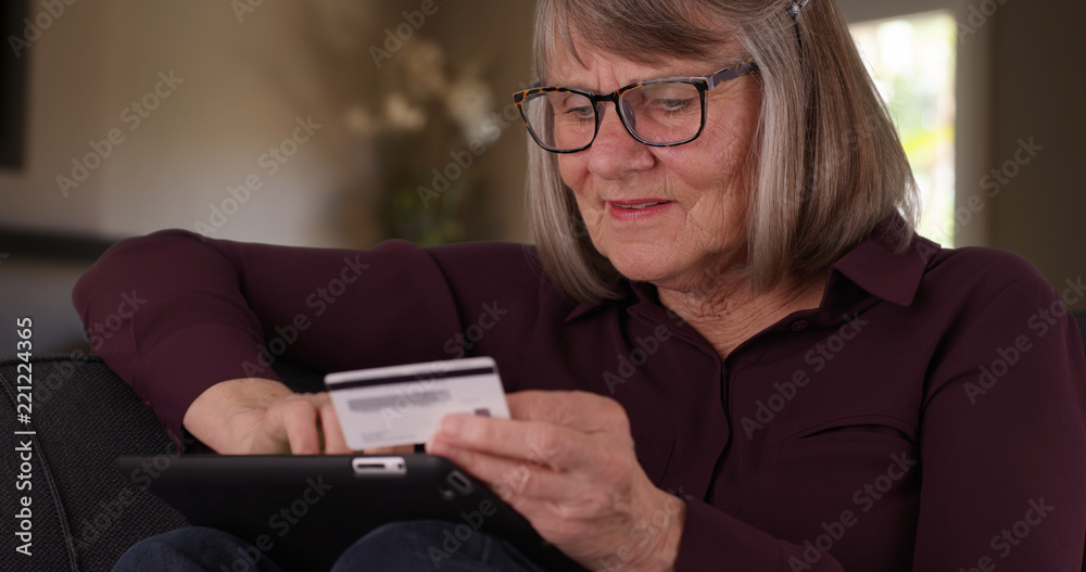 Close-up of cheerful old woman making online purchase on tablet sitting indoors