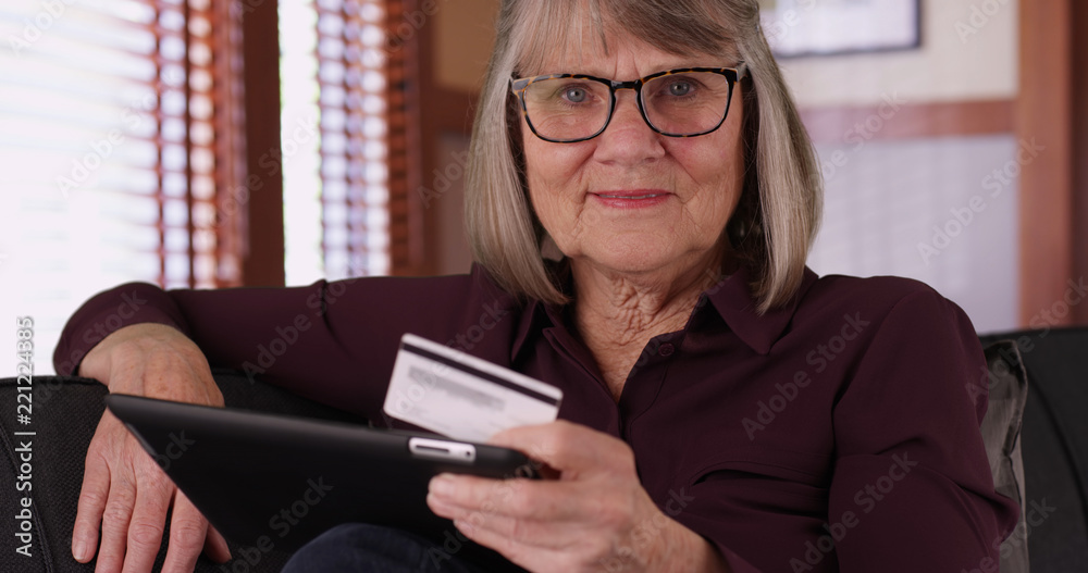 Close-up of older woman holding tablet and credit card looking at camera Close-up of older woman holding tablet and credit card looking at camera