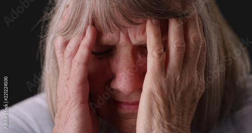 Tight shot of elderly woman with migraine headache rubbing head on gray backdrop