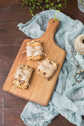 Homemade Chewy Granola Bars Wrapped in Parchment Paper and String on a Wood Cutting Board on Wood Table photo