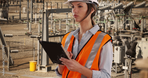 Focused female electrical worker at work on pad device at electrical facility