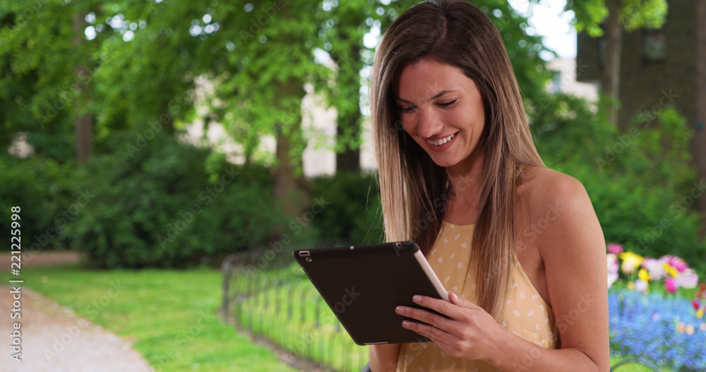 Happy white woman using tablet computer and smiling outside in public park Happy white woman using tablet computer and smiling outside in public park