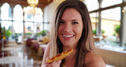 Close-up of happy woman eating pizza smiling at camera in restaurant setting