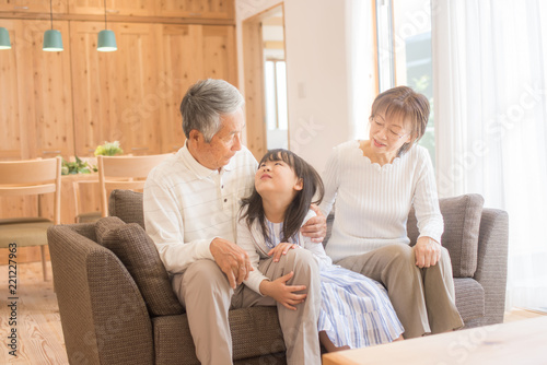 リビングのソファでくつろぐ孫娘とシニア夫婦 © tomoco_sozai