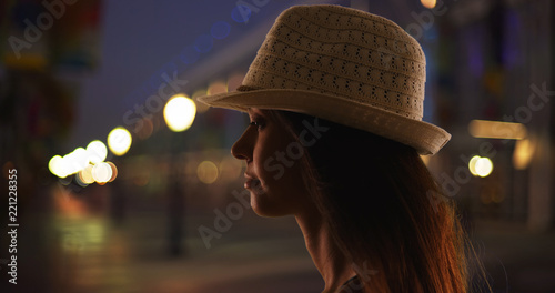 Close up silhouette of young woman in fedora standing on urban street at night
