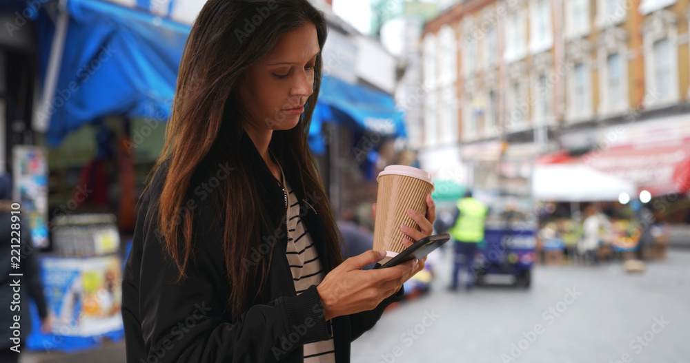 Hipster girl in bomber jacket texting with cell phone in London neighborhood Hipster girl in bomber jacket texting with cell phone in London neighborhood
