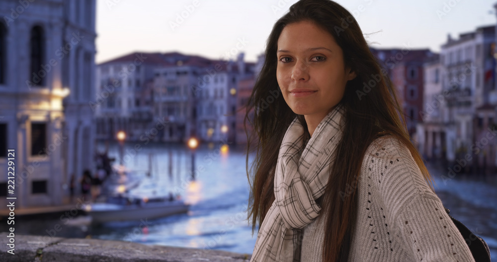 Millennial woman traveling in Italy smiles at camera by Grand Canal in evening Millennial woman traveling in Italy smiles at camera by Grand Canal in evening