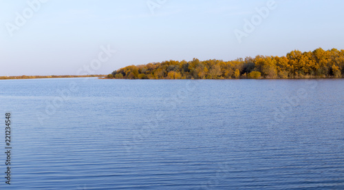 Landscape by the lake with a blue sky, yellow trees on the water with reflection