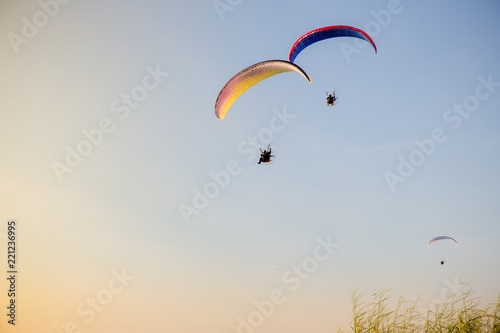 Guy flying on the clearly blue sky and wonderful beach by paramotor red kite, extreme activity port. feel freedom like birds. concept overcome the limits of human physiology.