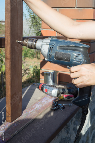 Woman hands drilling wood plank fence to metal construction. Building a wooden fence with a drill and screw. © Smole