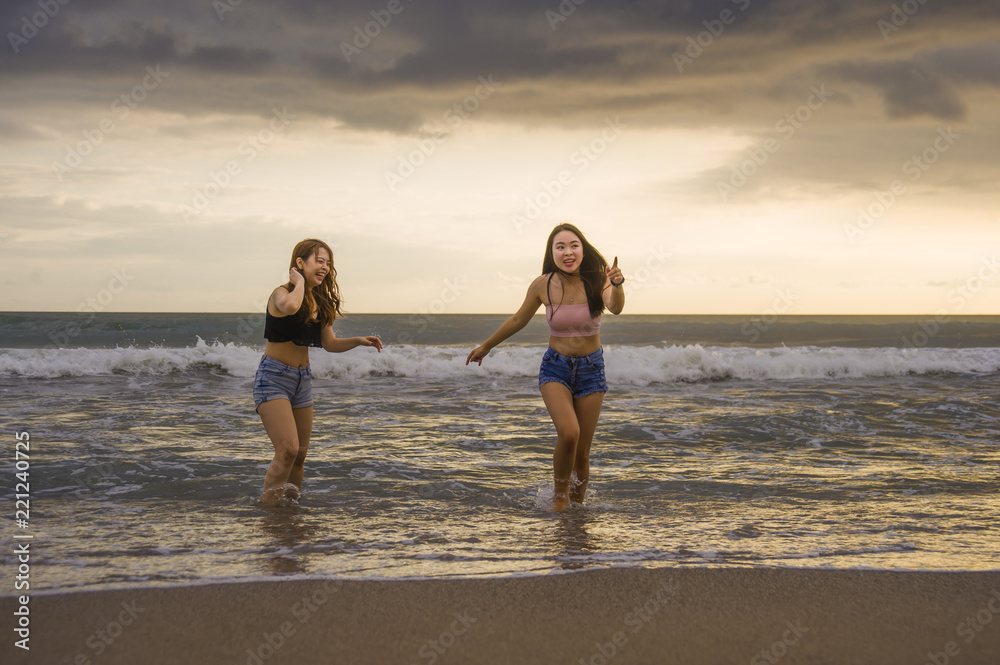 two happy and attractive young Asian Chinese women girlfriends or sisters having fun playing in the sea on sunset beach in beautiful light enjoying summer holidays two happy and attractive young Asian Chinese women girlfriends or sisters having fun playing in the sea on sunset beach in beautiful light enjoying summer holidays