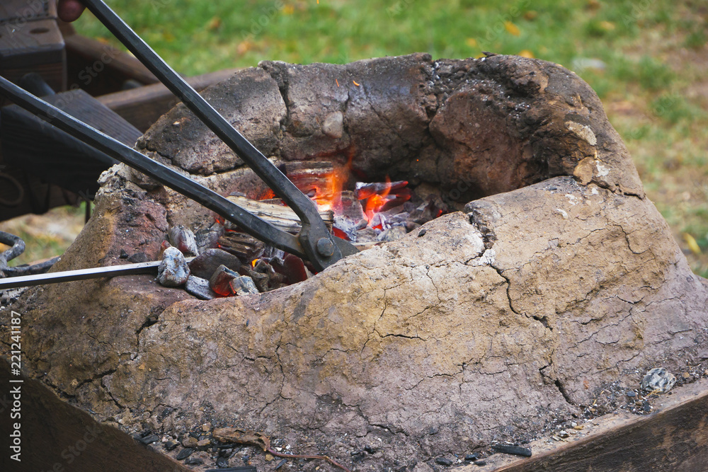Medieval furnace with iron tongs, burning coals and fire in blacksmith forge Medieval furnace with iron tongs, burning coals and fire in blacksmith forge