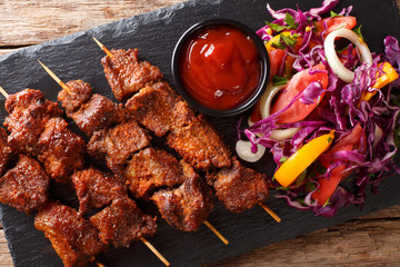 African food: spicy suya kebab on skewers with fresh vegetable salad and ketchup close-up. Horizontal top view