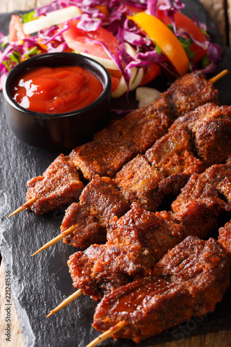 Suya- Roast African spicy skewered beef kebab is served with fresh vegetable salad and ketchup close-up. vertical