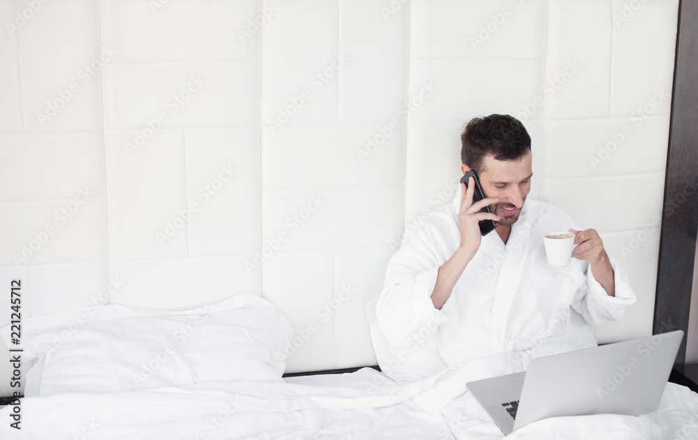 Happy handsome man using laptop in bed in the morning Happy handsome man using laptop in bed in the morning
