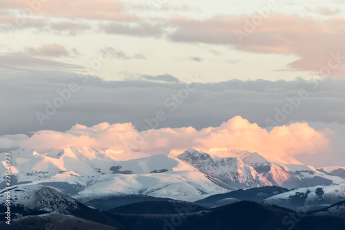 Mountain range covered by snow at sunset, with warm, purple shades reflections
