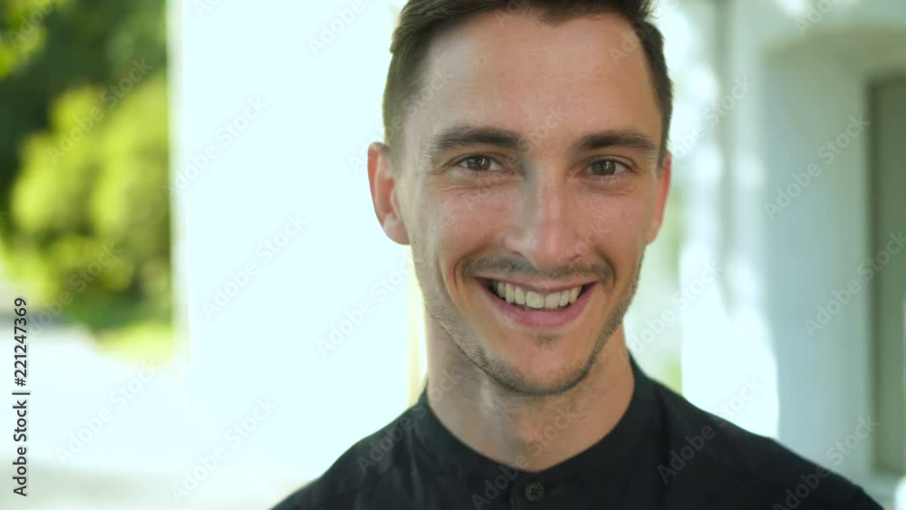 Attractive guy in city street on sunny day looking at camera. Smiling and laughing cute caucasian brunette man brunette Attractive guy in city street on sunny day looking at camera. Smiling and laughing cute caucasian brunette man brunette