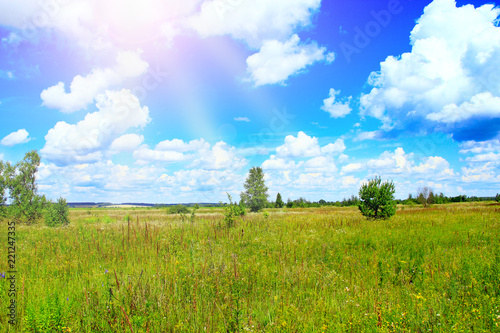 Summer landscape with sunny rays falling to field from white clouds on blue sky