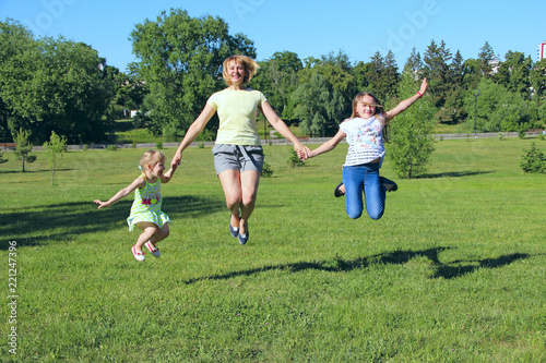 Happy mother having fun jumping with her daughters on green grass
