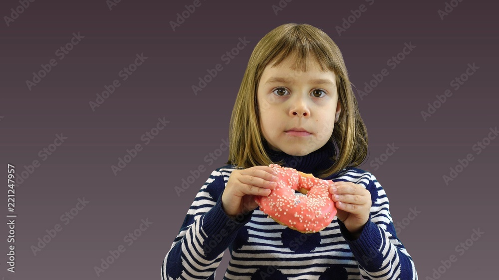Little girl is eating a donut on a colored background.