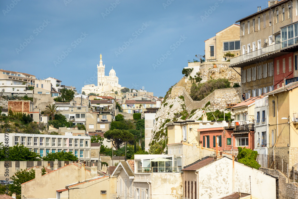 The immaculate basilica of Notre-Dame de la Garde in Marseille, France, on top of the hill seen from the Vallon des Auffes by a stormy summer day against a dark cloudy sky.