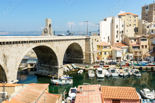 Fotografía View from above of the small fishing port of the Vallon des Auffes in Marseille, France, with traditional and modern boats, colorful cabanons, the bridge of the Kennedy corniche and the Orient gate
