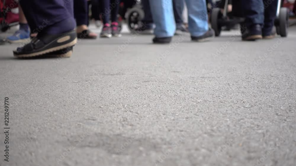Shoot from a low angle. A crowd of people is walking down the street. Legs in different shoes.