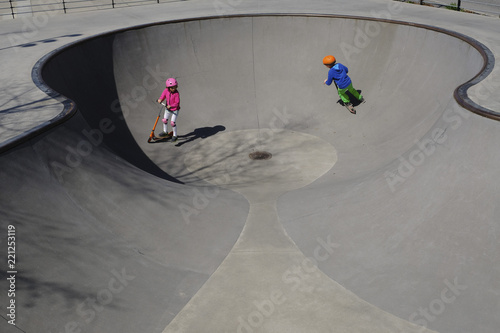 Brother and sister on scooters playing at sunny skate park photo