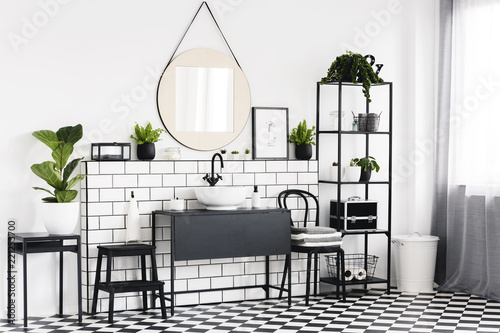 Plant on table in black and white bathroom interior with checkered floor and mirror. Real photo