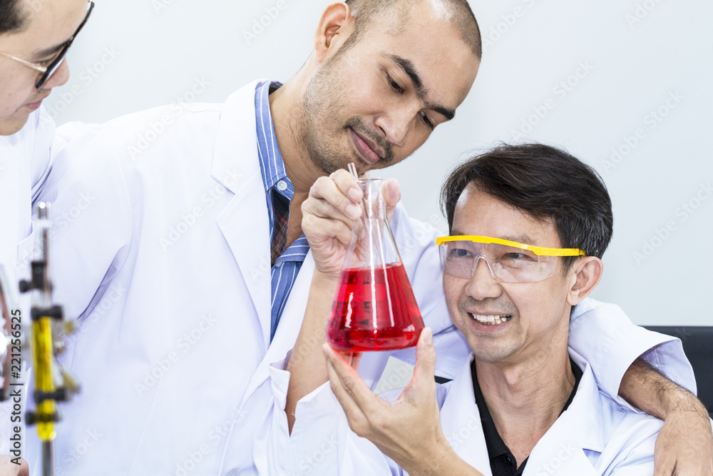 Portrait man of mature scientist and team in a white suit holding test tube at laboratory. Portrait man of mature scientist and team in a white suit holding test tube at laboratory.