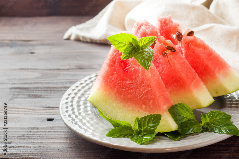 Watermelon sliced on a plate with mint leaves on a wooden background. Watermelon sliced on a plate with mint leaves on a wooden background.