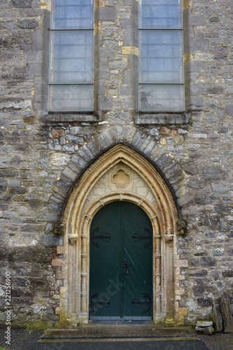 Arched dual door on metal hinges on side wall of stone medieval cathedral.