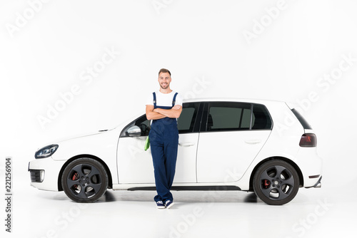 smiling handsome auto mechanic leaning on car with crossed arms on white photo