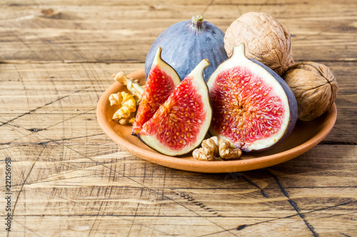 Fresh figs whole and cut kernels of walnuts on a plate the old wooden background.