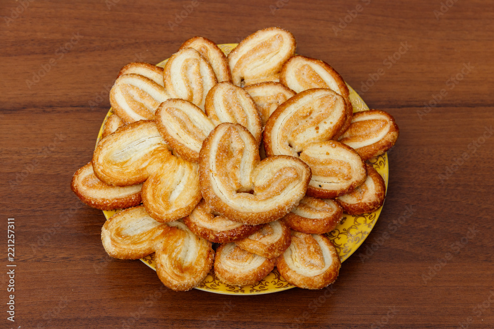 Palmier biscuits - french cookies made of puff pastry (also called palm leaves, elephant ears or french hearts) in a plate on wooden table Palmier biscuits - french cookies made of puff pastry (also called palm leaves, elephant ears or french hearts) in a plate on wooden table