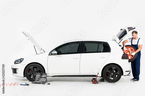 auto mechanic taking tire from car trunk on white