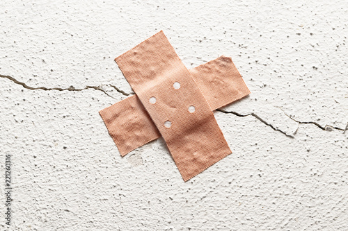 band-aid plaster in cross shape on a crack in the wall, concept for botched construction and doctoring around symptoms, copy space