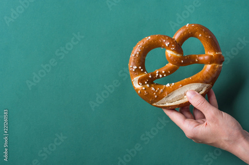 Fototapeta Young woman hold in hand German savory lye pretzel with salt on dark green background