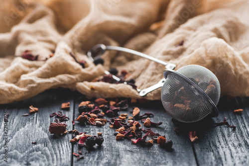 tasty black tea with dried fruits, tea strainer and cloth on wooden table photo