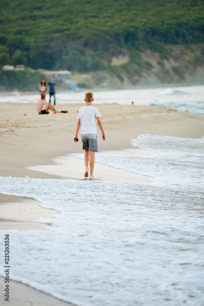 A boy in shorts is walking along the beach. Back view. A boy in shorts is walking along the beach. Back view.