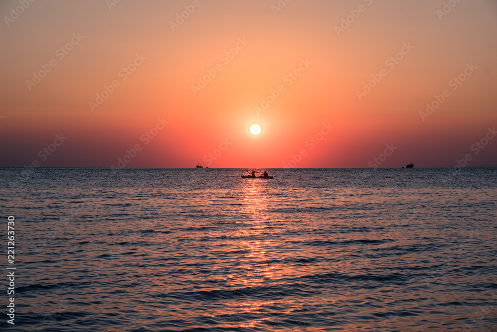 Rowing boat at the sea with orange sun setting over the horizon