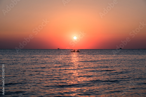 Rowing boat at the sea with orange sun setting over the horizon © Neeqolah