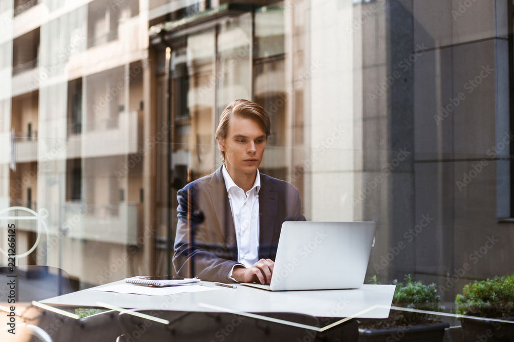 Business and the city. Handsome young man using his laptop while sitting in café outdoors