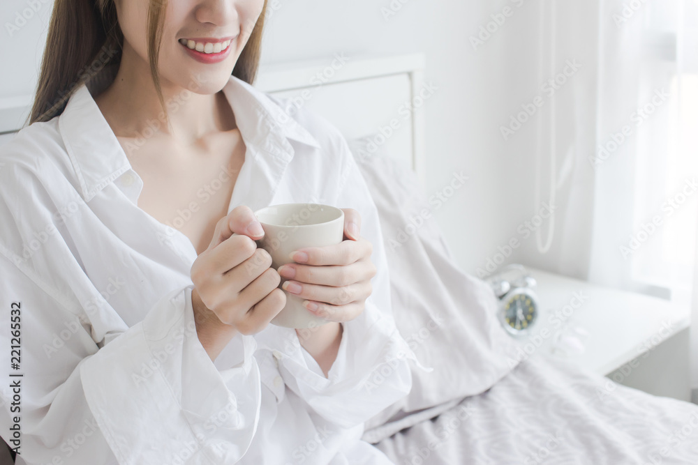 Close up of attractive Asian women in white shirt drinking coffee and smile in her bed