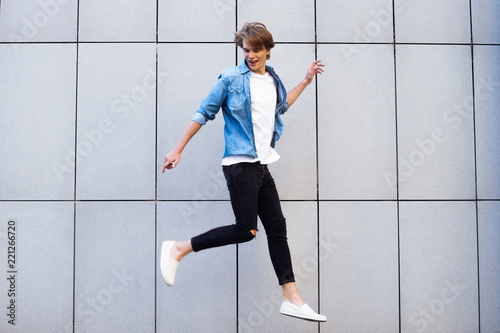 Funky style. Handsome young man looking away with smile while jumping outdoors