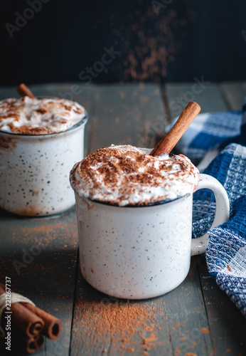 Hot cocoa with whipped cream and cinnamon stick on dark background
