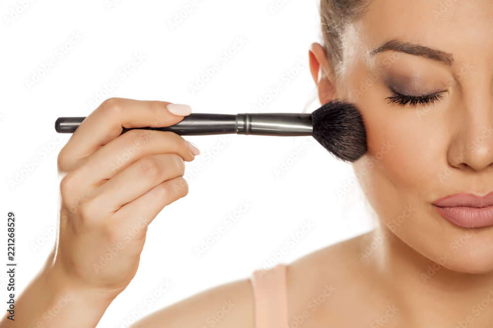 Young woman applying blush with brush on white background Young woman applying blush with brush on white background