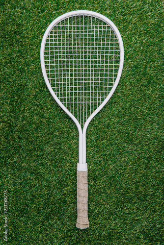 top view of white tennis racket lying on green grass