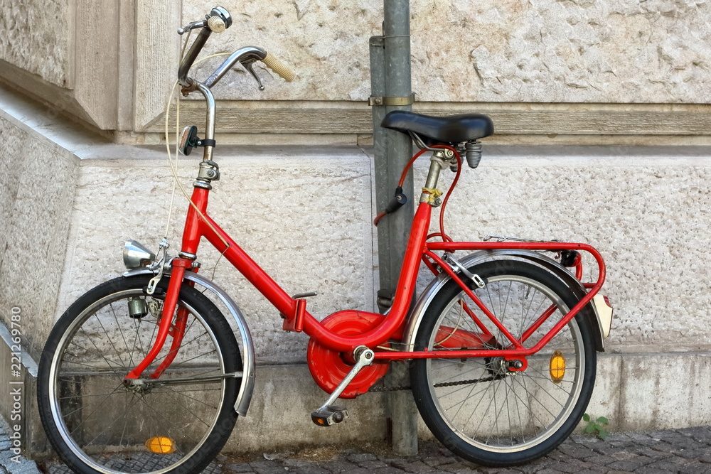bicicletta pieghevole vintage rossa appoggiata a muro